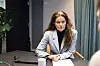 Kvinne i lys blazer sitter ved møtebord med dokumenter foran seg.