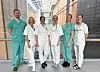 Gruppe helsepersonell i grønn og hvit bekledning poserer i lys sykehuskorridor.