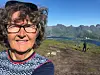 Person med briller tar selfie på fjelltopp med fjord og fjell i bakgrunnen