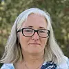 Kvinne med grått hår og briller står ute foran grønn, uskarp bakgrunn