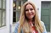 Kvinne med langt blond hår står foran bygård med grønne dører og vinduer.