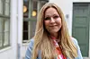 Kvinne med langt blond hår står foran bygård med grønne dører og vinduer.