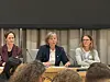 Tre kvinner deltar i paneldebatt bak bord med mikrofoner i møtesal.