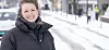 Smilende kvinne i mørk vinterjakke står ute i et snødekt bymiljø.