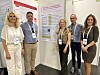 Fem personer poserer foran informasjonsplakater på en messestand.