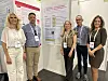 Fem personer poserer foran informasjonsplakater på en messestand.