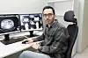 Mann sitter ved et skrivebord foran to dataskjermer med medisinske bilder på et kontor.