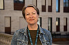 Smilende kvinne i denimjakke foran en moderne bygning.