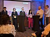 Paneldeltakere står ved høye bord på en konferansescene foran et publikum.