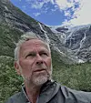 Eldre mann i forgrunnen foran et fossefall mellom bratte fjell.