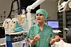 Helsearbeider i grønn operasjonsdrakt står i en operasjonsstue med medisinsk utstyr og monitorer.