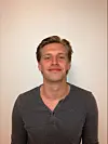 Person i mørk genser står foran en lys vegg og ser mot kamera.