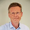 Portrett av en mann med briller og lys blå skjorte foran en lys bakgrunn.