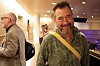 Smilende mann med gul skulderrem i en opplyst innendørs foajé.