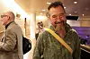 Smilende mann med gul skulderrem i en opplyst innendørs foajé.