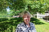 Smilende kvinne står i skyggen under et tre i en grønn park.
