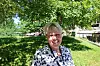 Smilende kvinne står i skyggen under et tre i en grønn park.