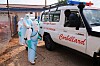 Helsearbeidere i hvitt verneutstyr desinfiserer en ambulanse merket med Colliard ved et sykehusområde.