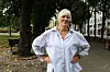 Kvinne i lys blå skjorte står på en parksti med trær og benker i bakgrunnen.