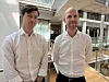 To menn i hvite skjorter står i et lyst kontoratrium med glassvegger.