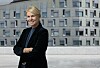 Smilende kvinne med korslagte armer foran en moderne grå bygning.