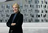 Smilende kvinne med korslagte armer foran en moderne grå bygning.