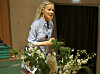 Berit Nordstrand står på en scene omgitt av blomster under en bokpresentasjon.