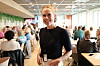 Smilende ansatt foran gjester i en lys og travel restaurant.