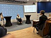 Paneldebatt med deltakere foran en skjerm og publikum i en konferansesal.