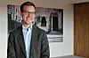 Smilende mann med briller i et moderne kontor med kunst på veggen.