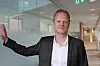 Mann i dress står ved en glassvegg i et lyst kontormiljø.