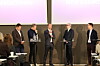 Fem personer deltar i en paneldebatt på en scene foran store skjermer.