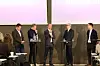 Fem personer deltar i en paneldebatt på en scene foran store skjermer.