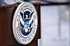 Seglet til U.S. Department of Homeland Security på et mørkt podium ved en flyplass.