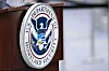Seglet til U.S. Department of Homeland Security på et mørkt podium ved en flyplass.